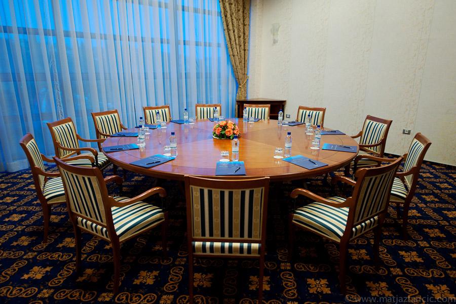 Grand Hotel Bernardin Portoroz Bagian luar foto The photo shows a conference room with a large round wooden table at its center. There are several wooden chairs arranged around the table, each with striped upholstery. On the table, there are folded blue napkins, water bottles, and a small floral c