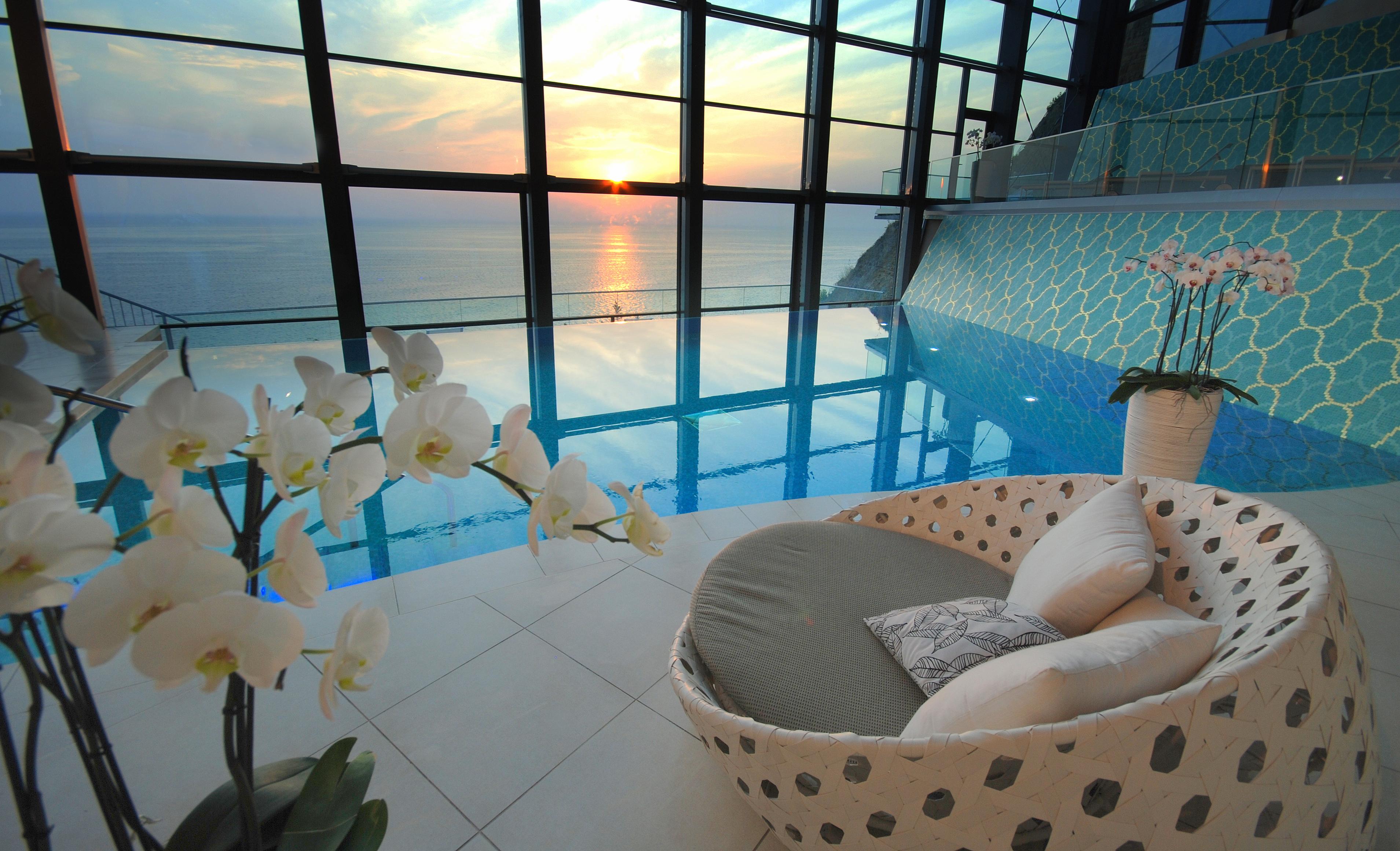 Grand Hotel Bernardin Portoroz Bagian luar foto The photo shows an elegant indoor space featuring a swimming pool with a panoramic view of the ocean at sunset. The pool reflects the colors of the sunset, creating a serene atmosphere. In the foreground, there is a comfortable, uniquely designed cha
