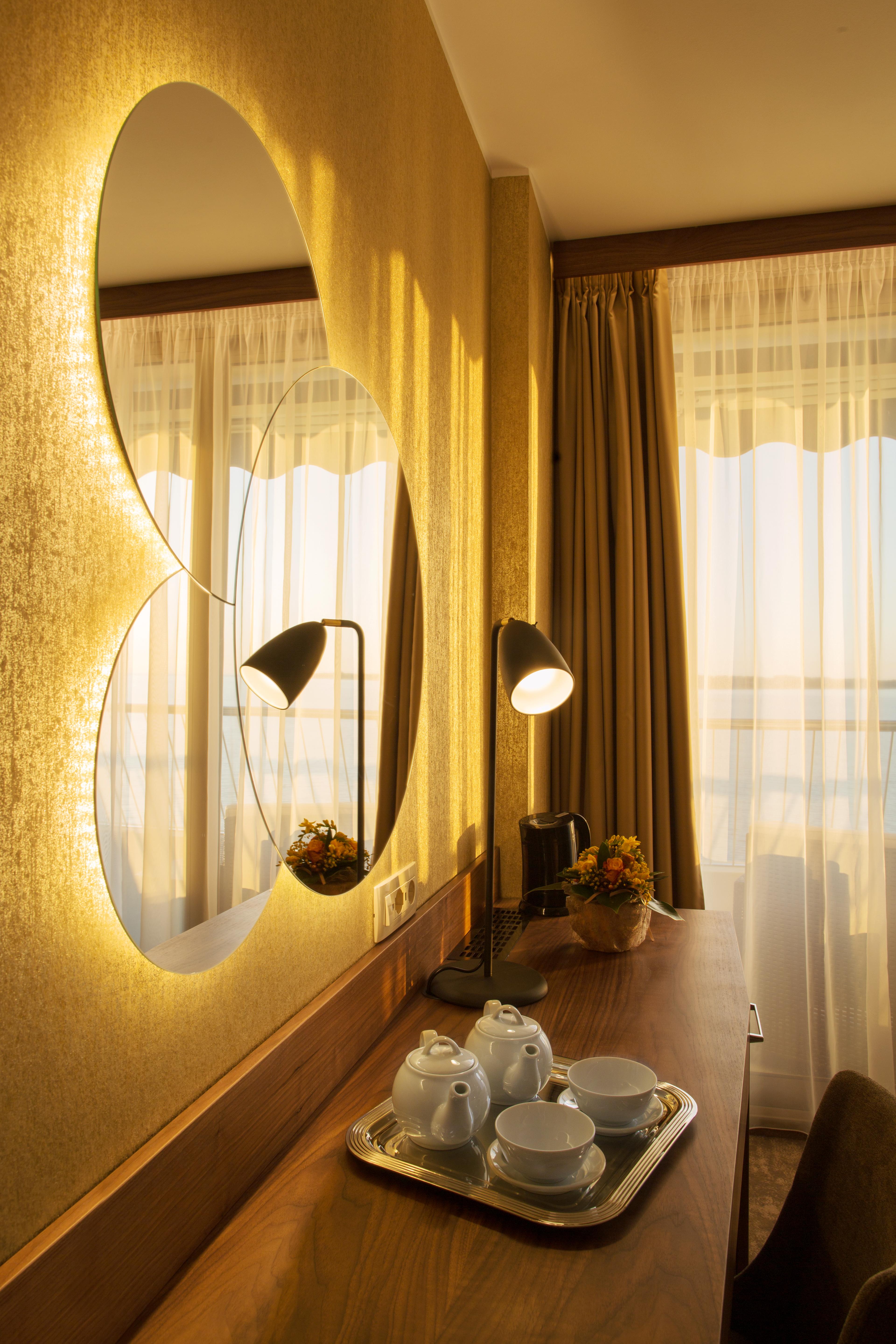Grand Hotel Bernardin Portoroz Bagian luar foto The photo features a cozy interior setting, likely from a hotel or a stylish room. There are two round mirrors on the wall, reflecting soft, warm light. A sleek black lamp sits on a wooden desk, providing additional illumination. Next to the lamp, th