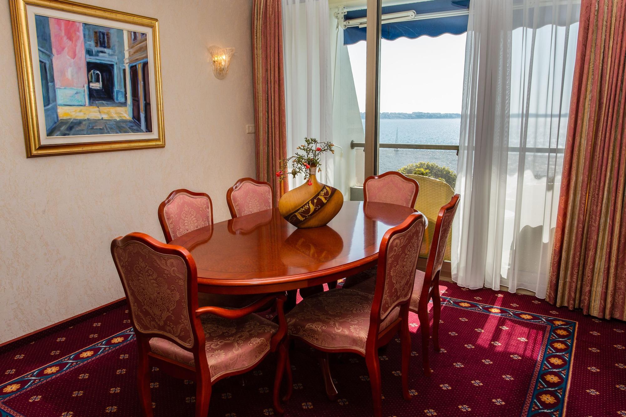 Grand Hotel Bernardin Portoroz Bagian luar foto The photo shows an elegant dining area with a wooden round table surrounded by six upholstered chairs. The chairs have a decorative pattern and are positioned around the table. A small vase with flowers sits at the center of the table. In the backgro