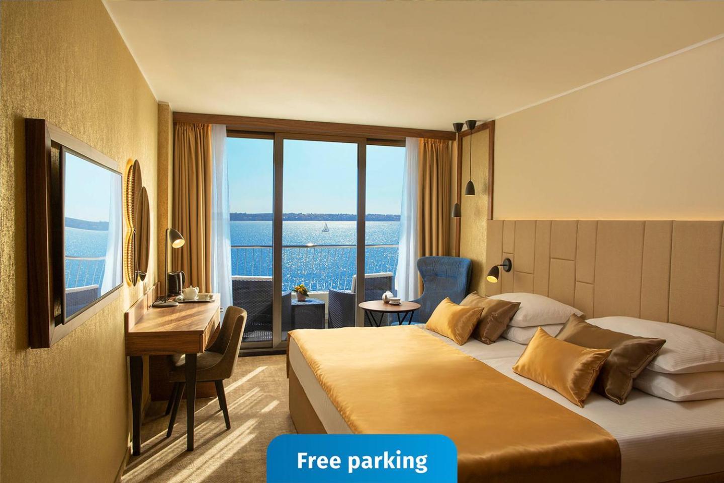 Grand Hotel Bernardin Portoroz Bagian luar foto The photo shows a modern hotel room featuring a large window with a view of the water. The room is decorated in warm tones, with a comfortable bed that has gold-colored bedding. There is a desk and chair situated next to the window, as well as a wall