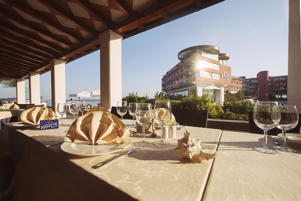Grand Hotel Bernardin Portoroz Bagian luar foto The photo depicts a dining setup at a restaurant, featuring elegantly arranged tables on a terrace. Each table is covered with a light-colored tablecloth and has an artistic napkin folding resembling a flower. There are several empty wine glasses and
