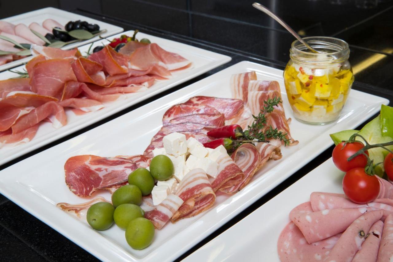 Grand Hotel Bernardin Portoroz Bagian luar foto The photo shows a selection of charcuterie and accompaniments arranged on white plates. There are various types of cured meats, including slices of ham and salami, presented attractively. In the center, there are green olives and pieces of cheese, al