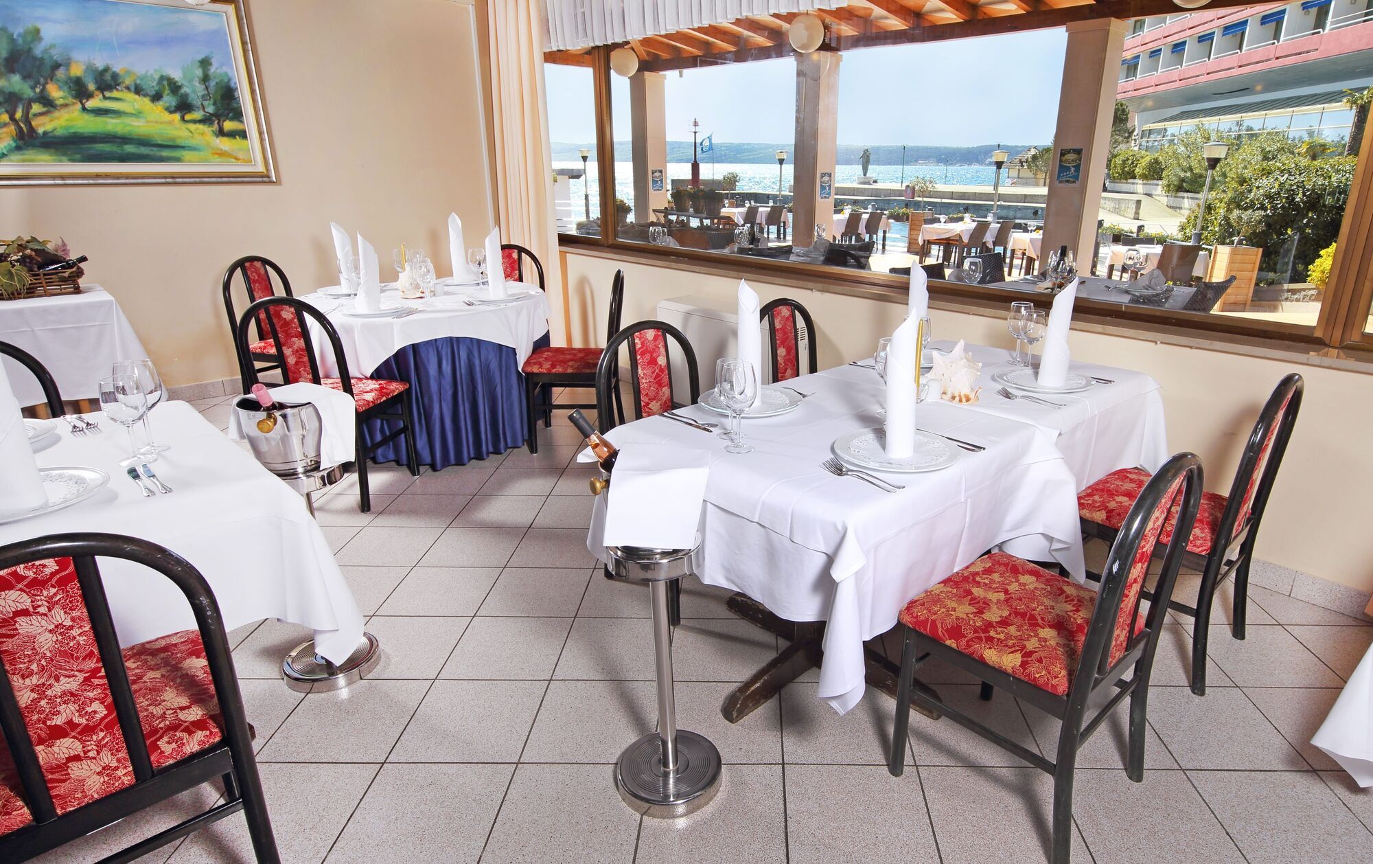 Grand Hotel Bernardin Portoroz Bagian luar foto The photo shows the interior of a dining area in a restaurant. There are several tables, each covered with white tablecloths. The chairs are a mix of black frames with either floral or solid-colored cushions. Large windows provide a view of the outsi